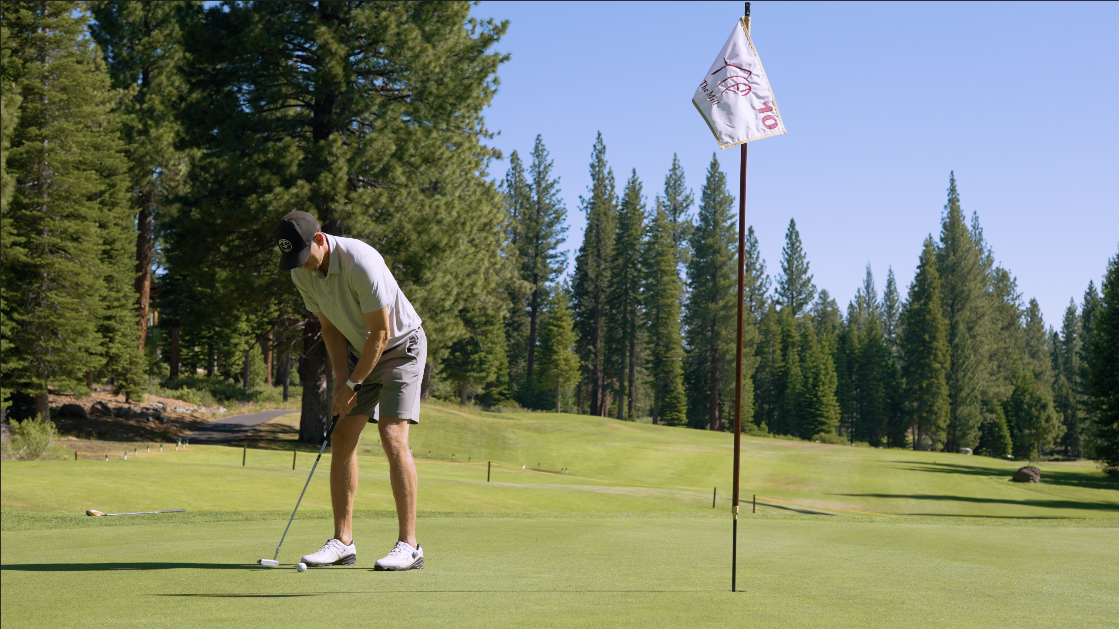 This image showcases a well-maintained golf course, a desirable amenity for potential homeowners. A golfer is seen putting on the green near the flag, highlighting the course's playability. The scene is set against a backdrop of trees and clear skies, creating an inviting and upscale environment.