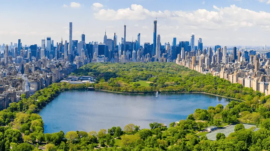 This image showcases an aerial view of Central Park and the surrounding cityscape of New York City. The park's lush greenery and the lake contrast beautifully with the dense urban environment and towering skyscrapers. This view emphasizes the property's proximity to a major park and desirable urban amenities.