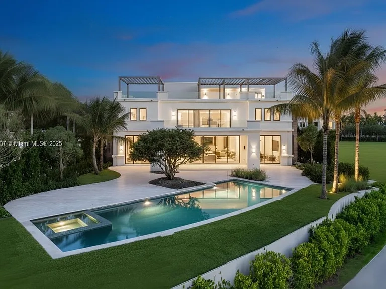 The rear exterior showcases a luxurious home featuring a swimming pool and attached spa. The bright white facade of the house stands out against the manicured lawn and palm trees. Large glass doors offer views into the interior, creating an inviting atmosphere for outdoor living and entertaining.