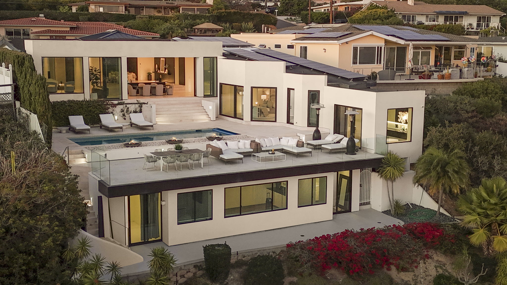 This modern, multi-level coastal residence features an expansive outdoor living area, complete with a swimming pool, a spacious patio deck, and a lounge space overlooking scenic surroundings. The sleek, contemporary architecture includes floor-to-ceiling windows, white stucco walls, and refined outdoor furniture, creating a sophisticated and luxurious atmosphere. Its structured layout and integrated amenities make it an exceptional example of high-end, indoor-outdoor California living.