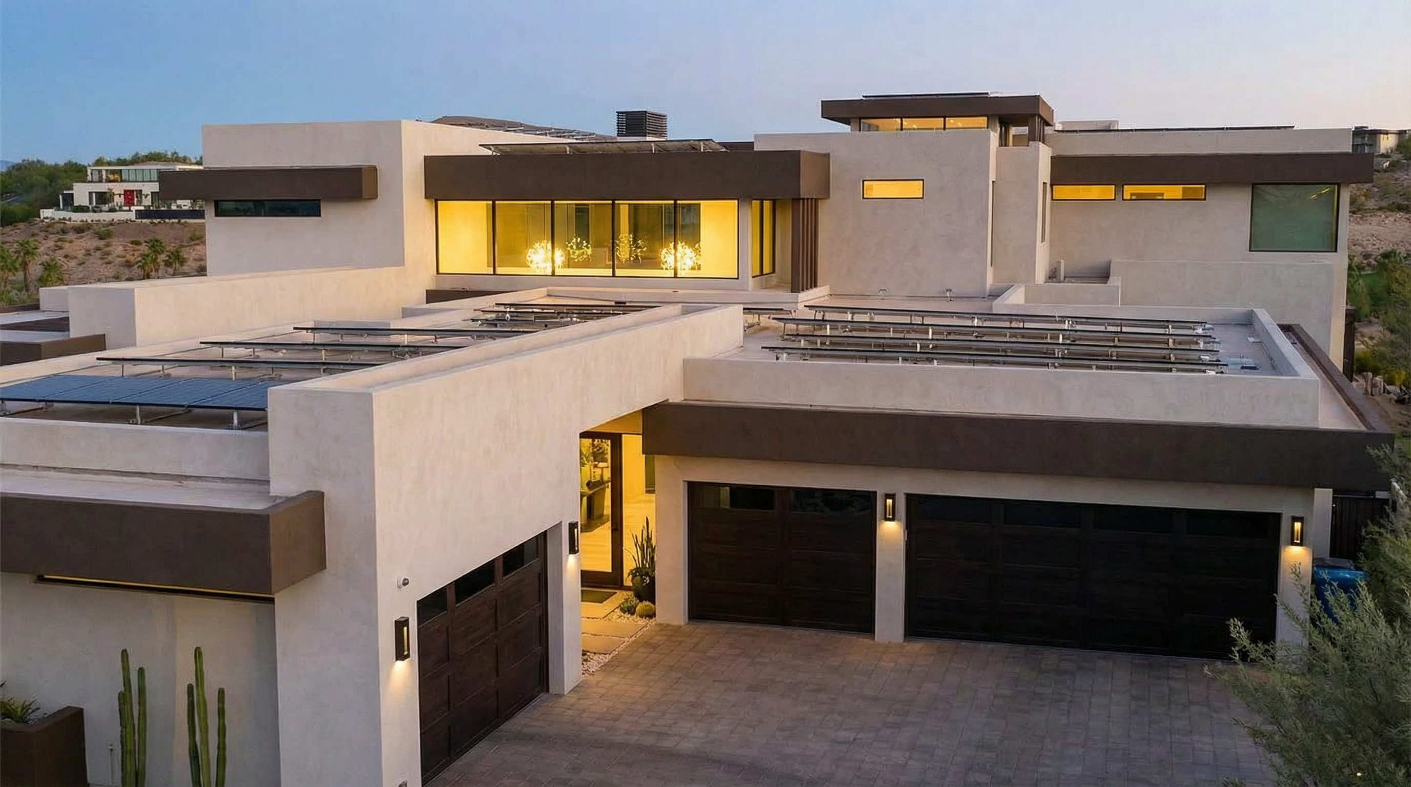 This is a stunning front view of a modern, multi-level home. The architectural design features flat roofs, a stucco exterior, and dark-trimmed windows that provide visual contrast. Solar panels are visible on the roof, indicating energy efficiency.