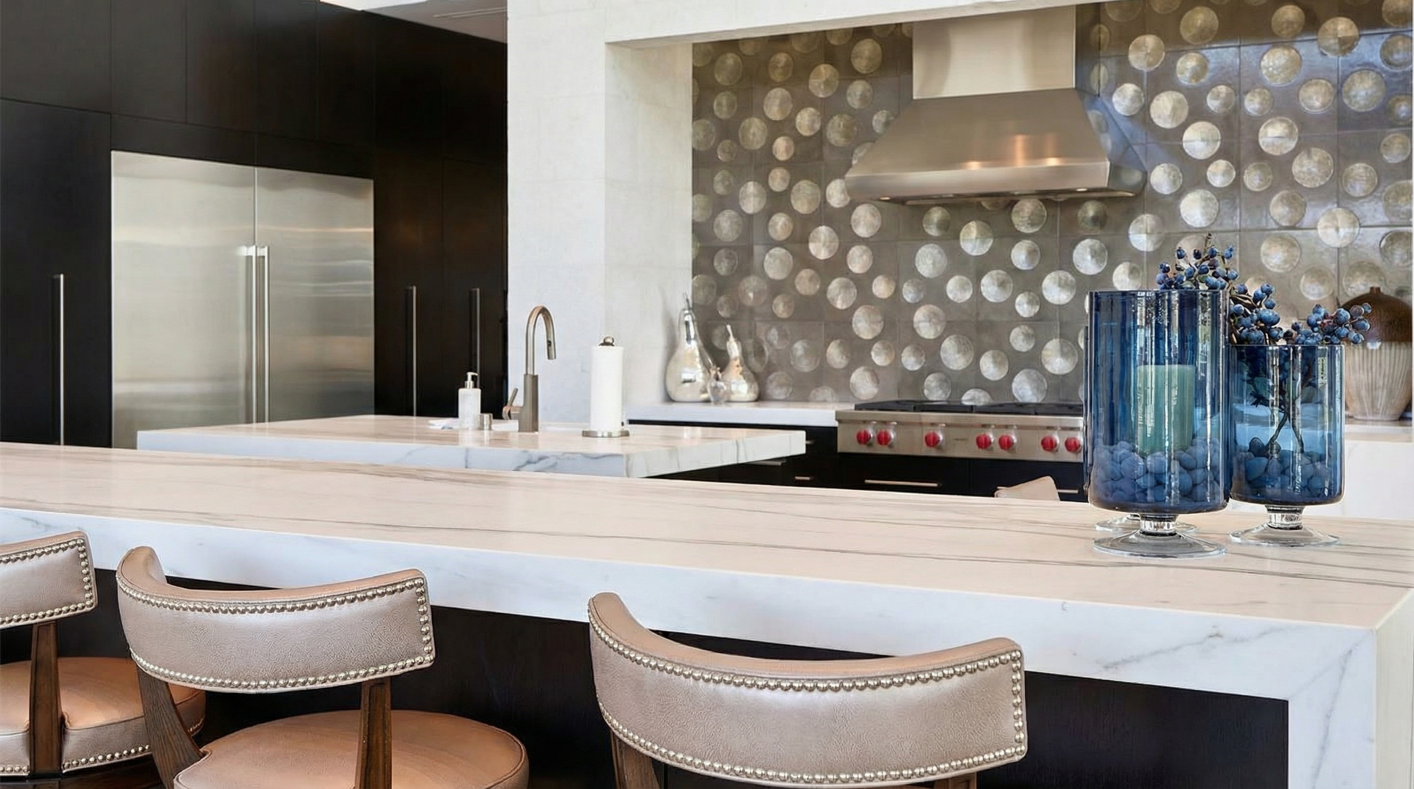 The picture showcases a modern kitchen with a luxurious aesthetic. The focus is on the elegant white marble countertops, complemented by the neutral-toned bar stools. High-end appliances and stylish backsplash tiles contribute to the kitchen's upscale feel, making it a desirable feature for potential homebuyers.