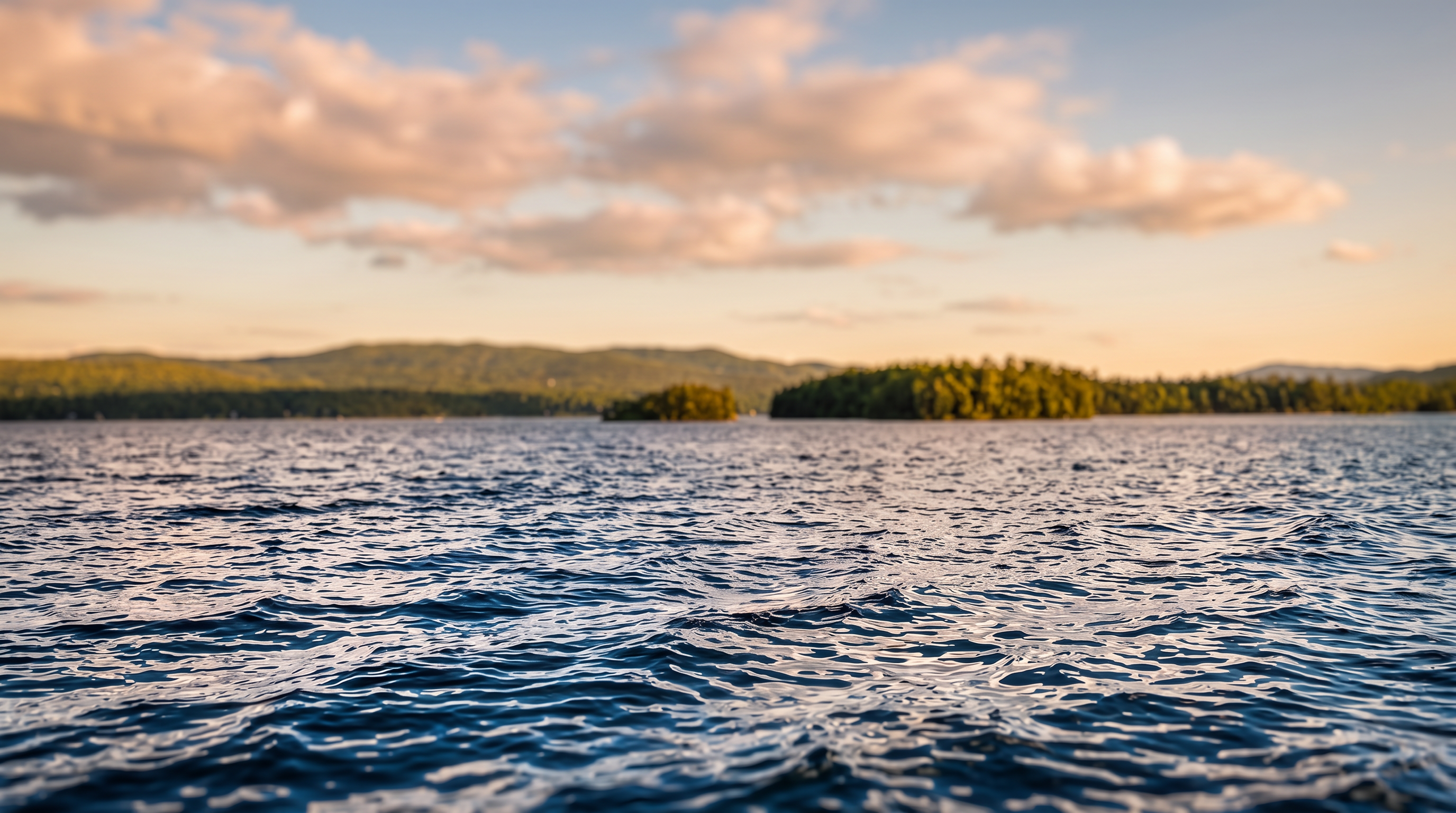 This image shows a scenic view of a body of water with distant wooded shorelines and islands during golden hour. The peaceful, natural aesthetic would be an appealing feature for a waterfront property listing, highlighting the natural beauty and tranquility of the location.