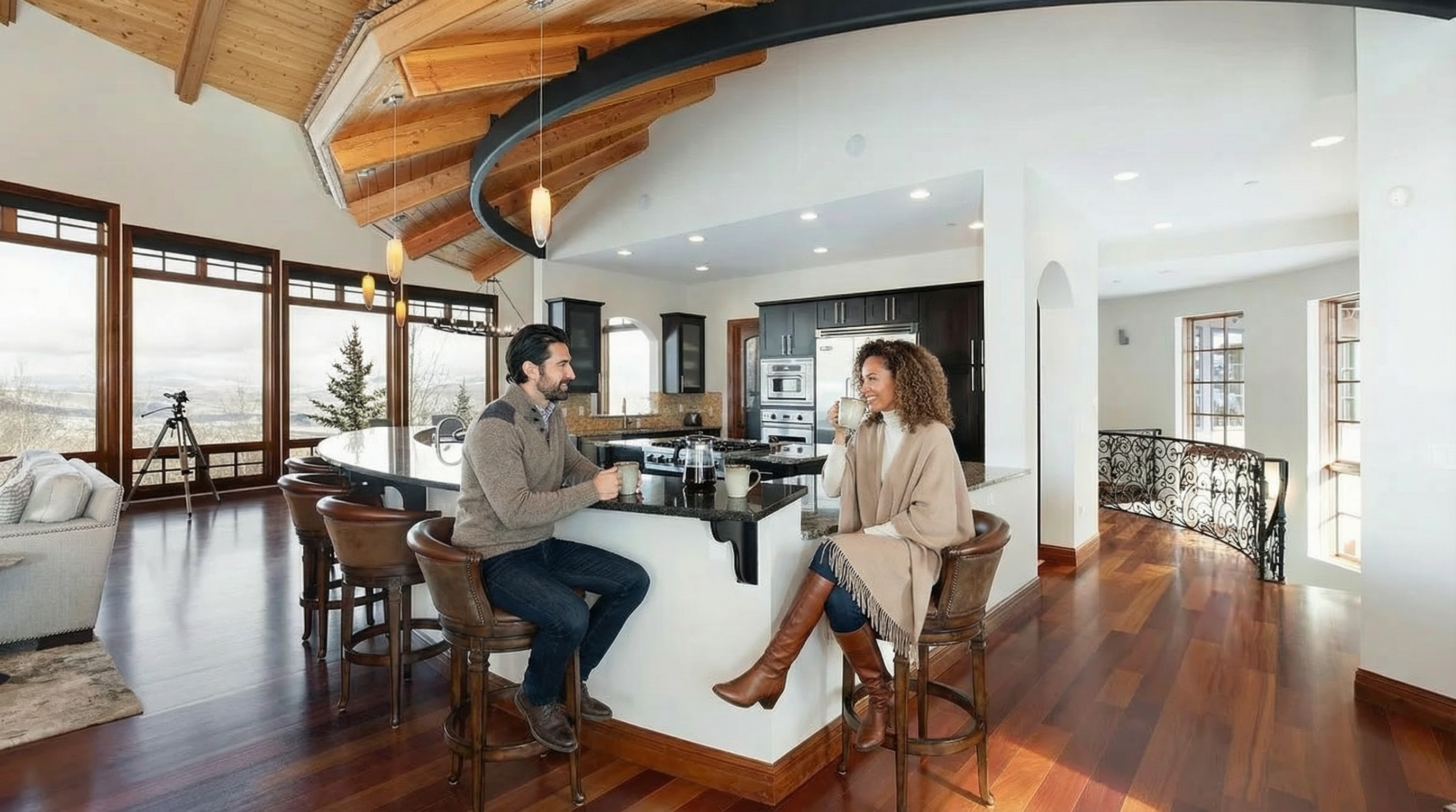 This spacious kitchen features dark wood cabinets, stainless steel appliances, and a large island with seating. Natural light floods the area through large windows, offering scenic views. The open floor plan and warm wood flooring create an inviting atmosphere.