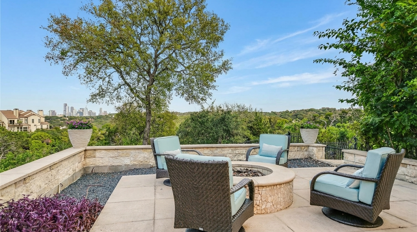 This image showcases a well-appointed outdoor patio area. Four wicker chairs with light blue cushions surround a stone fire pit, creating a cozy gathering space. The patio is paved with stone tiles and overlooks a lush green landscape, suggesting a tranquil and private setting perfect for relaxation or entertaining.