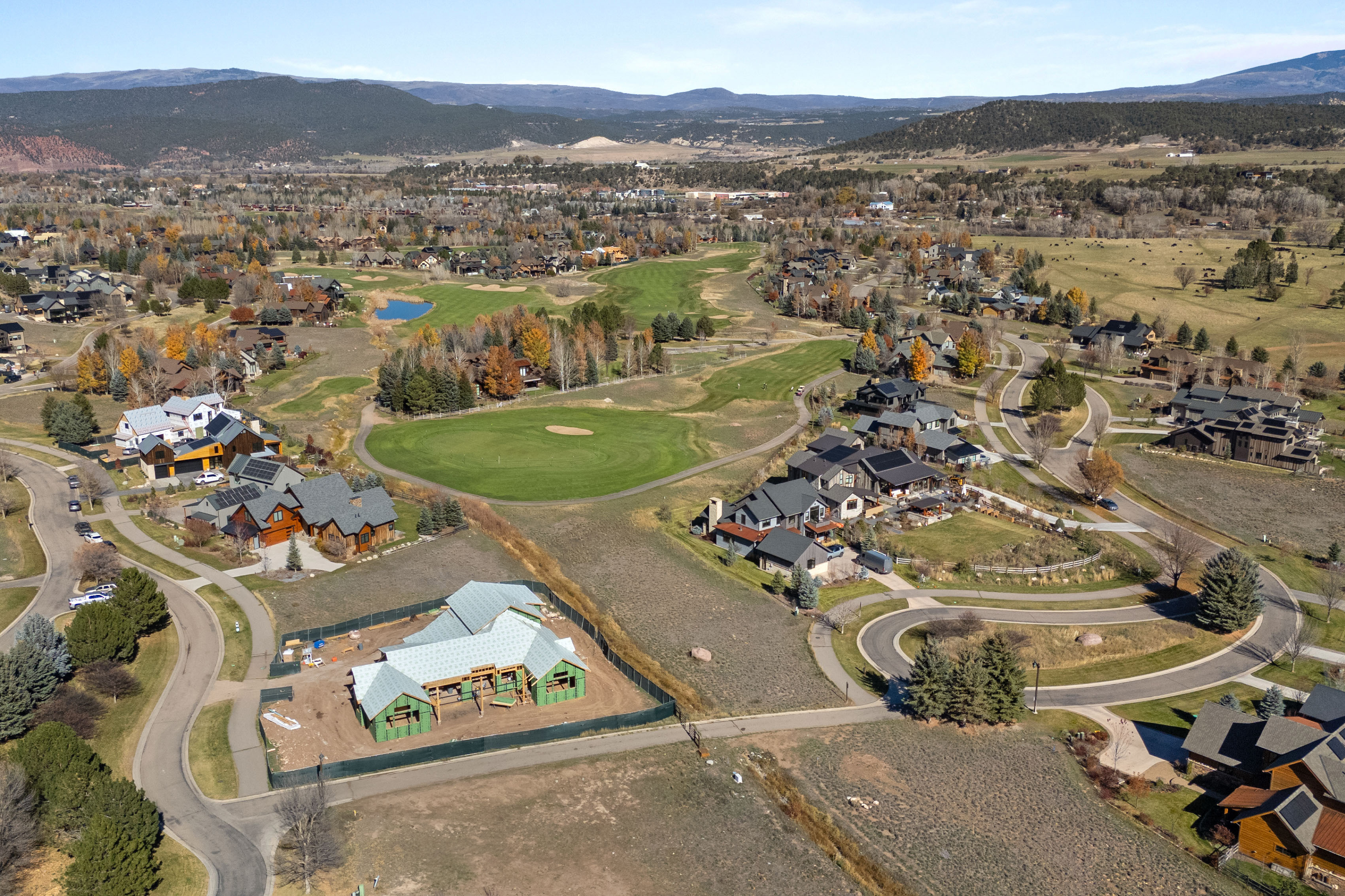 This high-angle aerial view captures a luxury residential community set against a backdrop of rolling hills and mountains. The neighborhood features a mix of completed high-end homes and a new construction project, all integrated seamlessly into a well-maintained golf course landscape. The scene highlights the spacious, master-planned nature of the community, emphasizing curb appeal, scenic views, and ample green space.