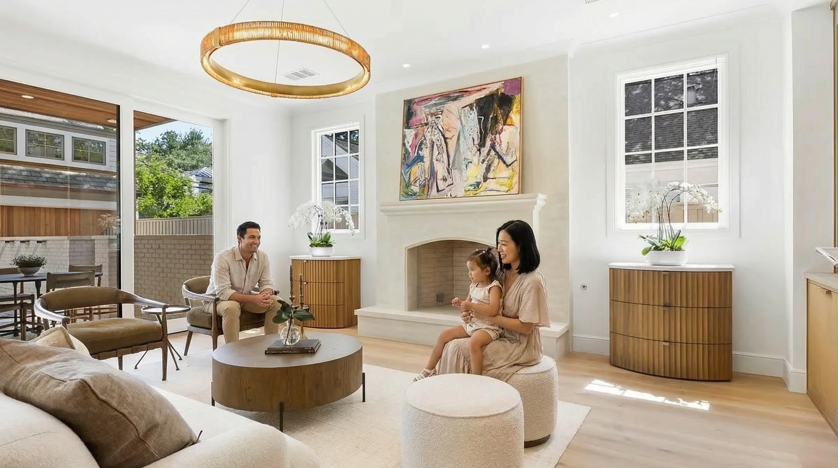 This is a bright and airy living room showcasing a circular chandelier, a modern fireplace with an abstract painting above, and contemporary furniture. The room features large windows that let in ample natural light, and the light wood flooring adds to the overall warmth. The design is elegant and inviting, perfect for family gatherings.
