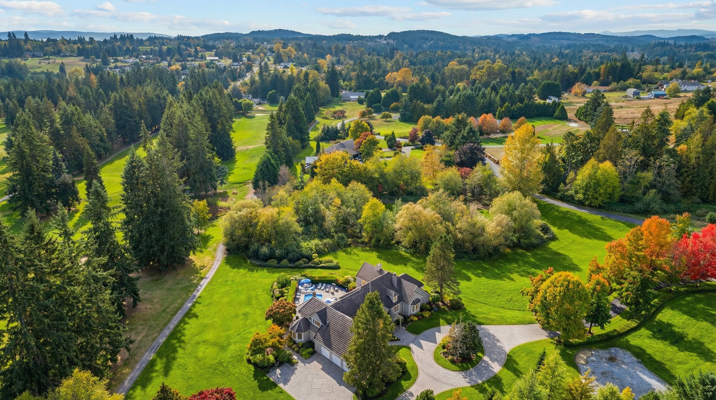 This aerial shot showcases an expansive estate featuring a meticulously-landscaped lawn, mature trees, and a spacious house with an attached garage. The property boasts a pool and a well-designed driveway leading up to the residence. Its setting in a lush, green environment creates an impression of privacy and luxury.
