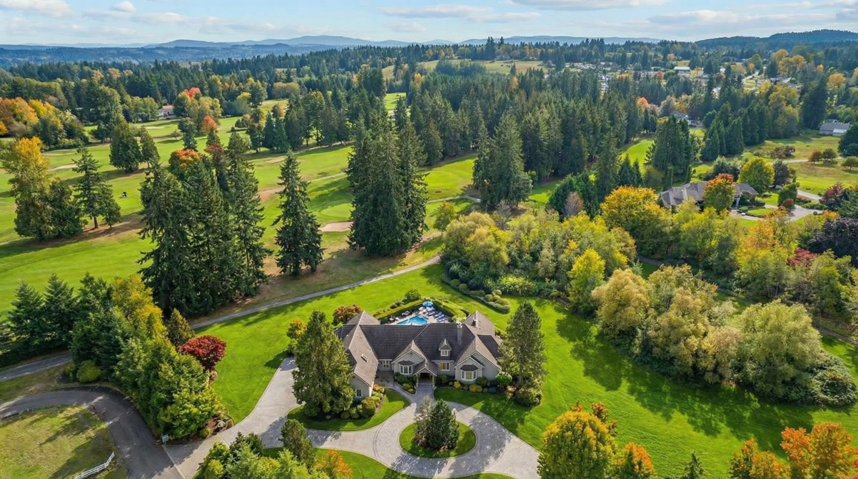 An aerial view reveals a luxurious estate situated on a manicured golf course. The property boasts a sprawling lawn and a private swimming pool, surrounded by mature trees and lush landscaping. The home features a beautifully designed circular driveway, adding to the overall appeal and exclusivity of the property.