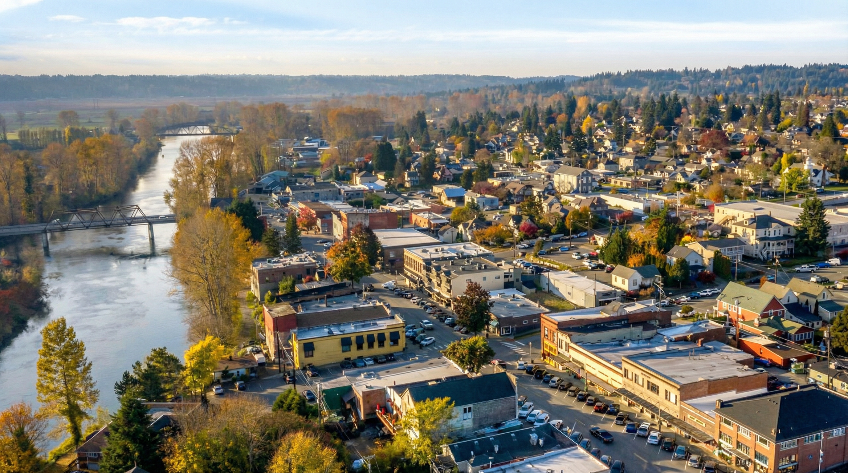 This aerial view showcases a charming town nestled alongside a river, ideal for highlighting the location and community feel. The image emphasizes the town's proximity to natural surroundings, with lush trees and waterways creating a picturesque setting. Buildings are a mix of residential and commercial, showcasing a vibrant downtown area.
