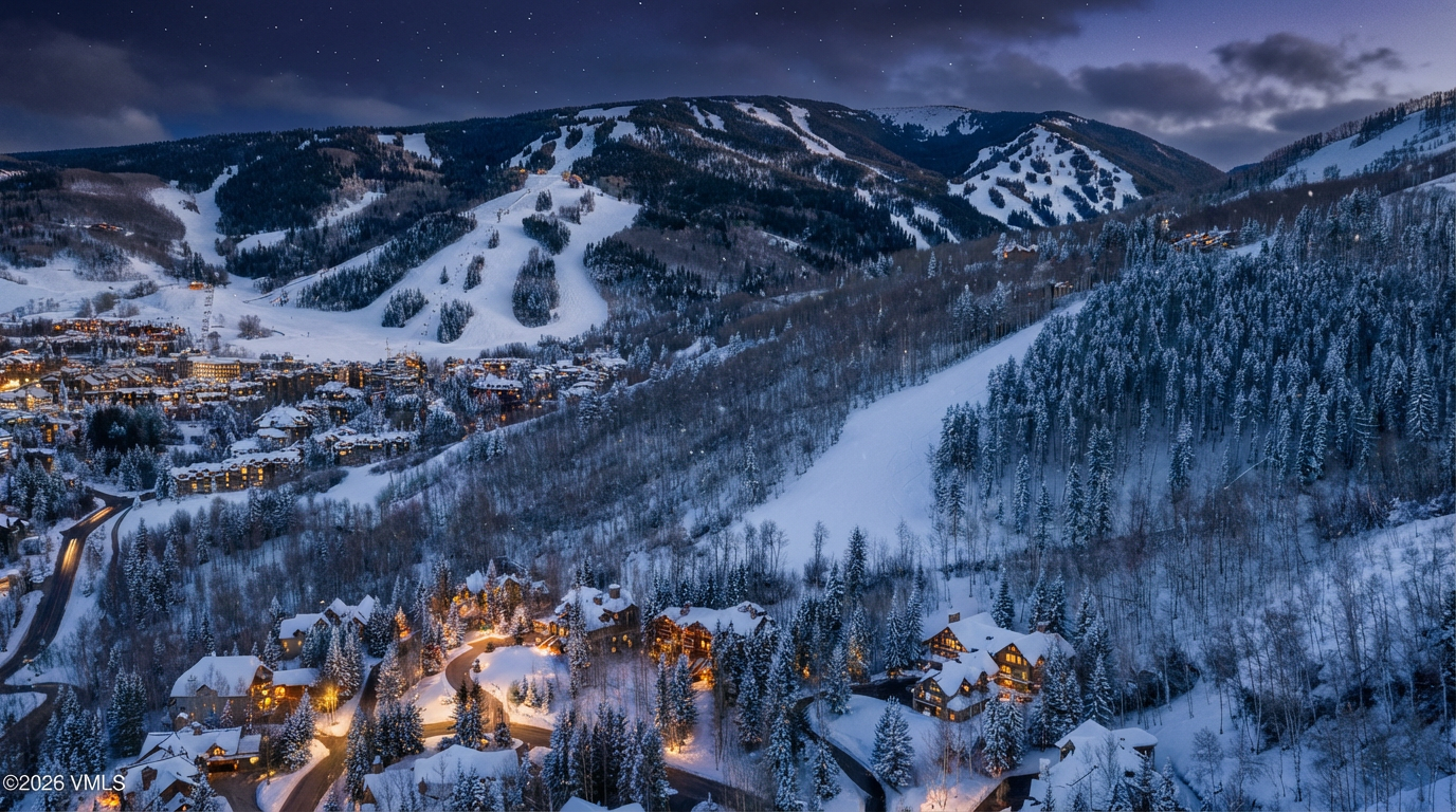 This is an aerial view of a mountain resort town at dusk showcasing luxury homes illuminated with warm interior lights. Snow-covered trees and ski slopes dominate the landscape, suggesting the property's prime location for winter sports enthusiasts. The image captures a serene and upscale ambiance, ideal for highlighting the desirability of the real estate in the area.
