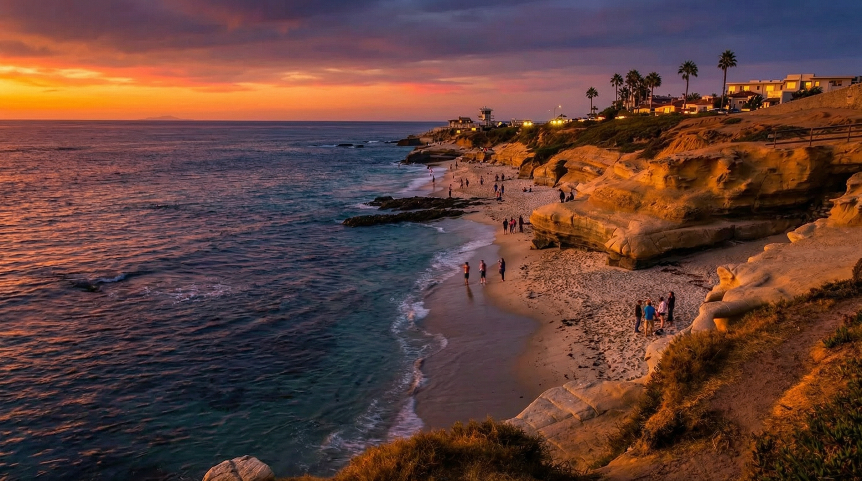 This image showcases a stunning coastal property at sunset. The side view reveals the beach below, accessible from the cliffs, with people enjoying the scenery. Above, residential buildings are visible, suggesting a desirable location with beautiful ocean-side scenery.