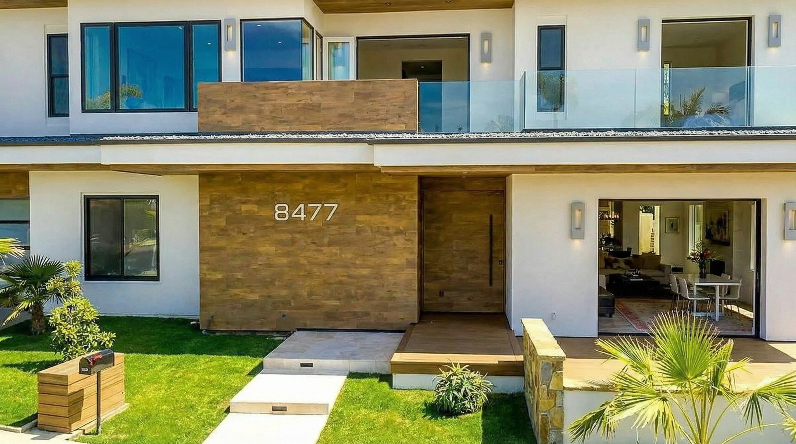 The image showcases the front exterior of a modern home with a striking facade. Key features include a combination of smooth stucco, wood paneling, and large windows. The design incorporates a balcony with glass railing, enhancing the property's curb appeal and giving it a luxurious feel.