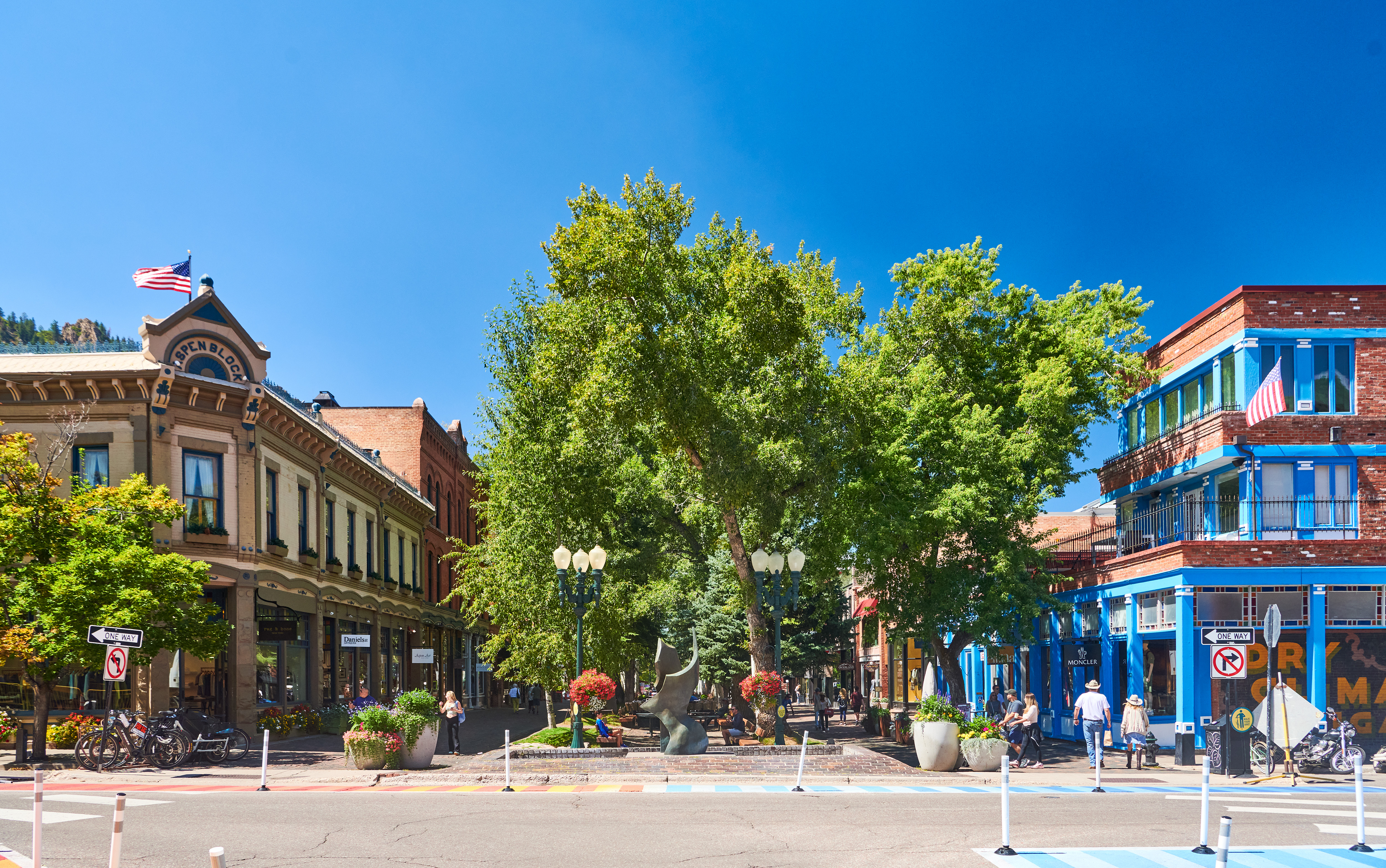 This image displays a vibrant, pedestrian-friendly downtown area in a historic mountain town. The scene features well-maintained storefronts, mature green trees, and public plazas that enhance the walkability and charm of the commercial district. The inviting atmosphere, coupled with iconic architecture and proximity to retail and dining, highlights a highly desirable and scenic urban environment.
