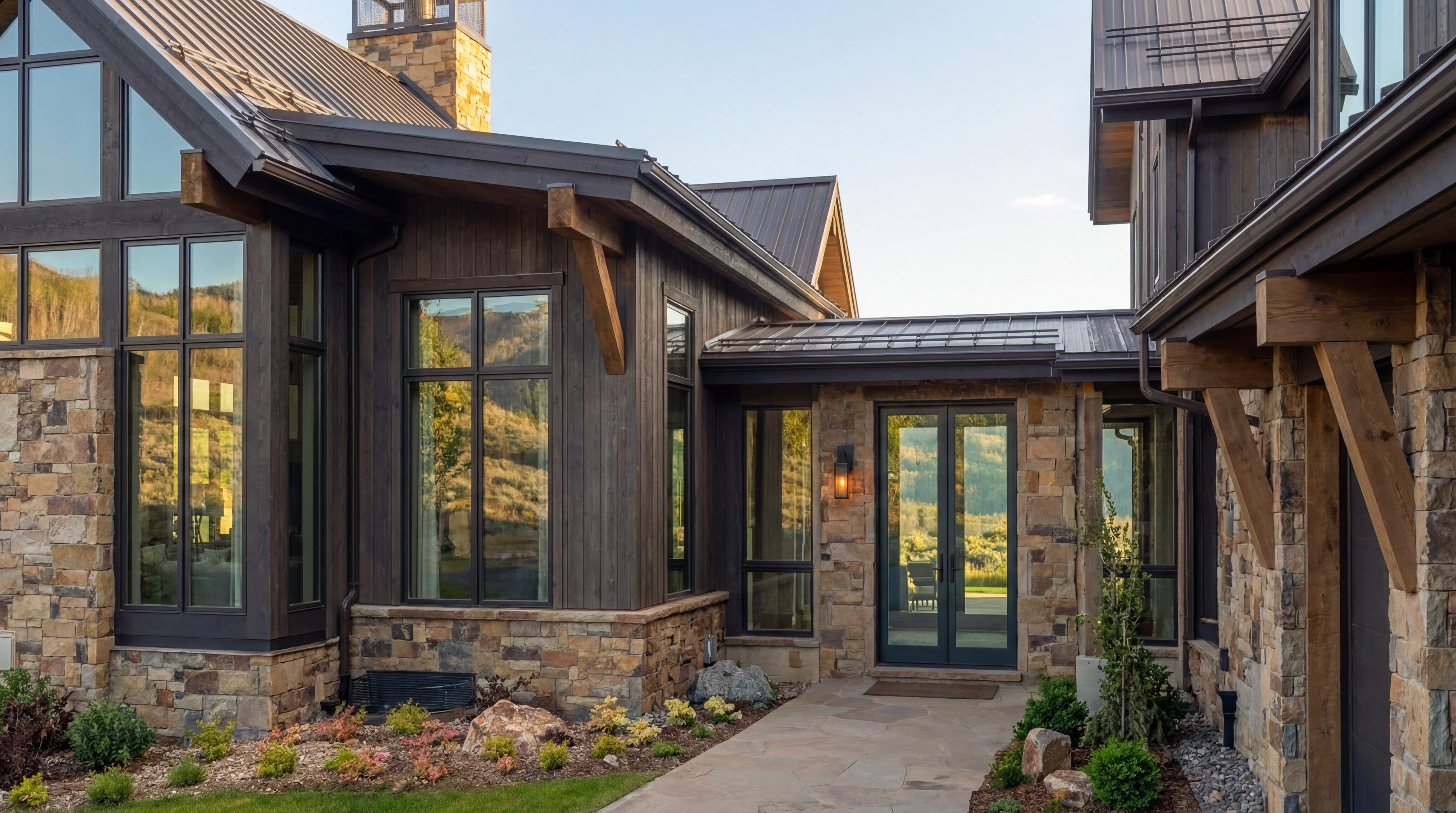 This stunning mountain-style home features a charming entryway highlighted by stone veneer, wood siding, and natural timber accents. The entrance boasts glass-paneled double doors, a flagstone walkway, and thoughtful landscape design, creating a warm and rustic-modern aesthetic. The reflective windows showcase the surrounding natural beauty, offering an inviting and high-end curb appeal.