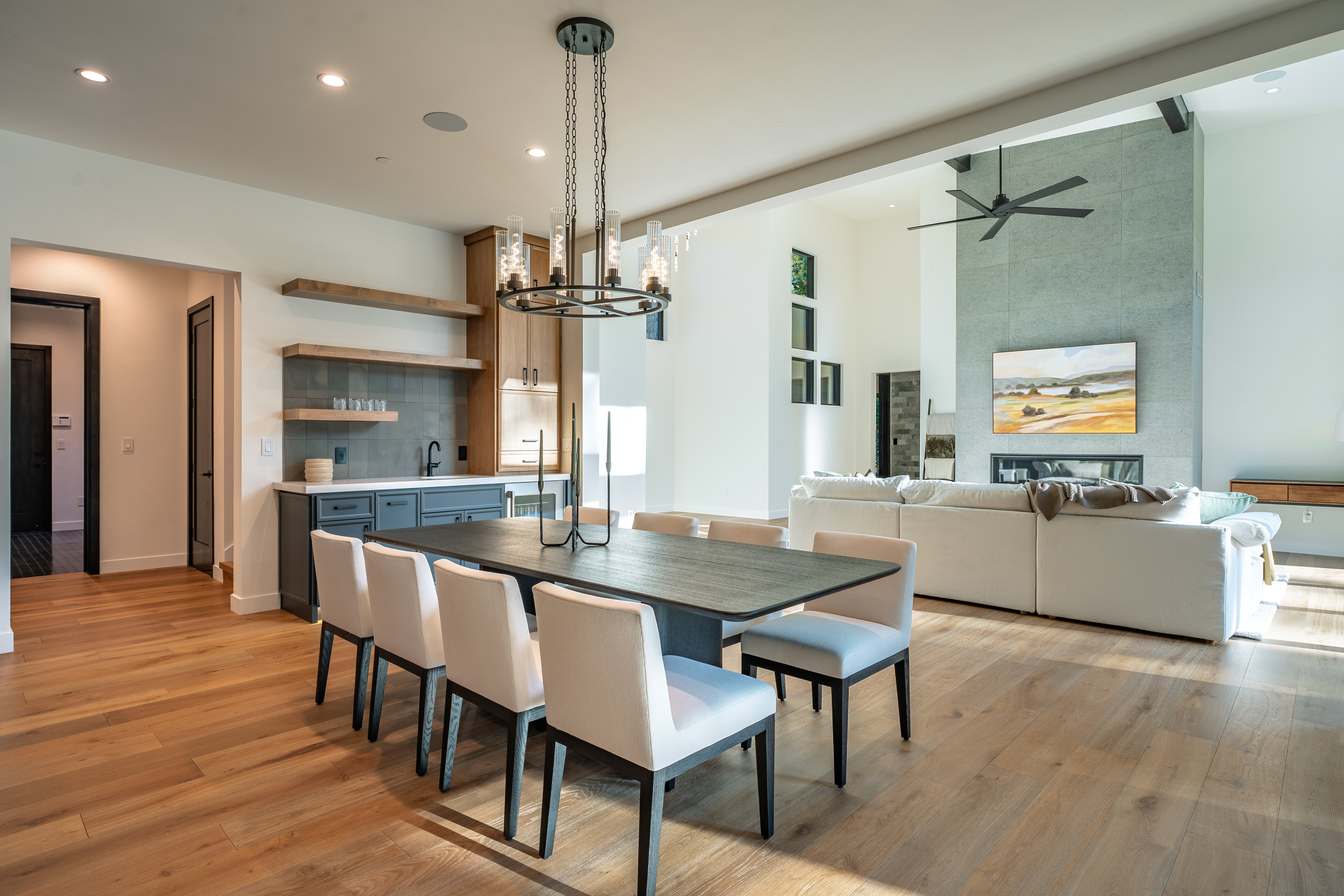 This interior shot showcases a modern dining room that seamlessly flows into the living area. The dining room features a dark wood table surrounded by upholstered chairs, illuminated by a contemporary chandelier. The adjacent living room boasts a large sectional sofa and a striking fireplace with a stone surround, creating an open and inviting space perfect for entertaining.