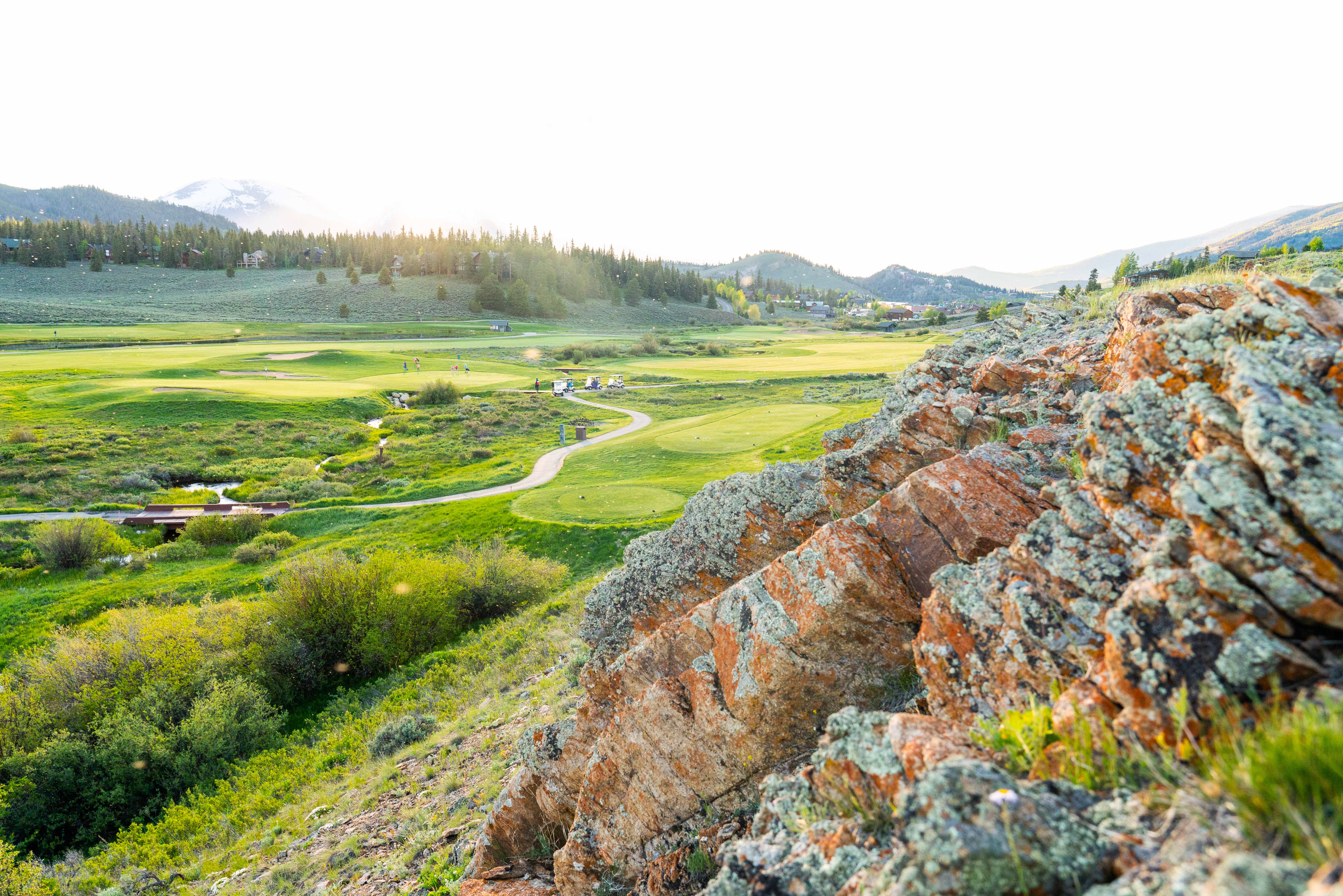 This image showcases a beautifully maintained golf course with rolling green hills, winding pathways, and scenic views of surrounding mountains and forests. The photograph highlights the community's outdoor recreational amenities and tranquil setting. This picturesque landscape offers potential homeowners a glimpse of the active lifestyle opportunities available in the area.
