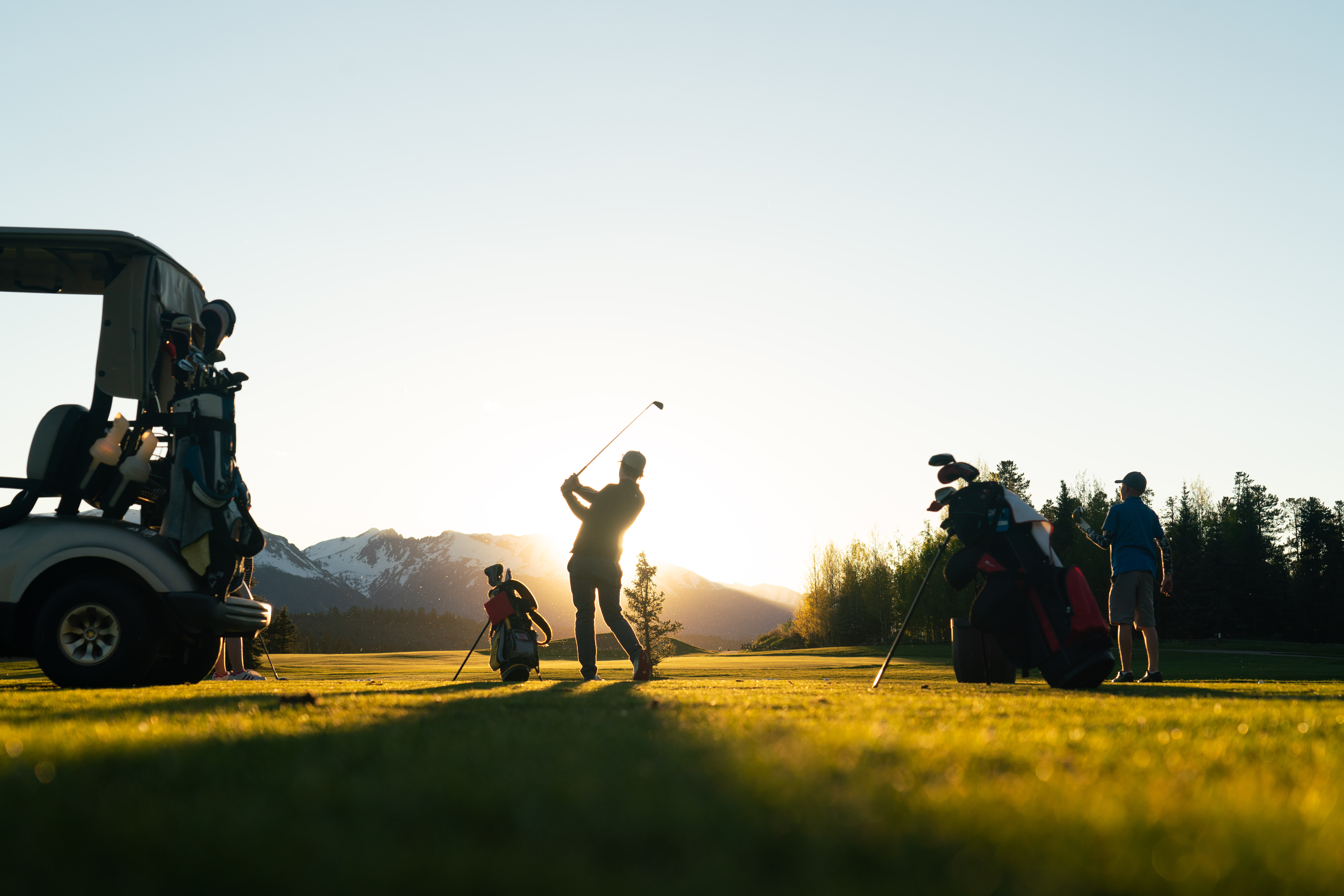 This image showcases a golf course at sunset, featuring individuals playing golf. The scene includes golf carts and golf bags, emphasizing the active lifestyle and recreational opportunities available. The backdrop of mountains and lush greenery adds to the appeal, portraying an idyllic and upscale community amenity.