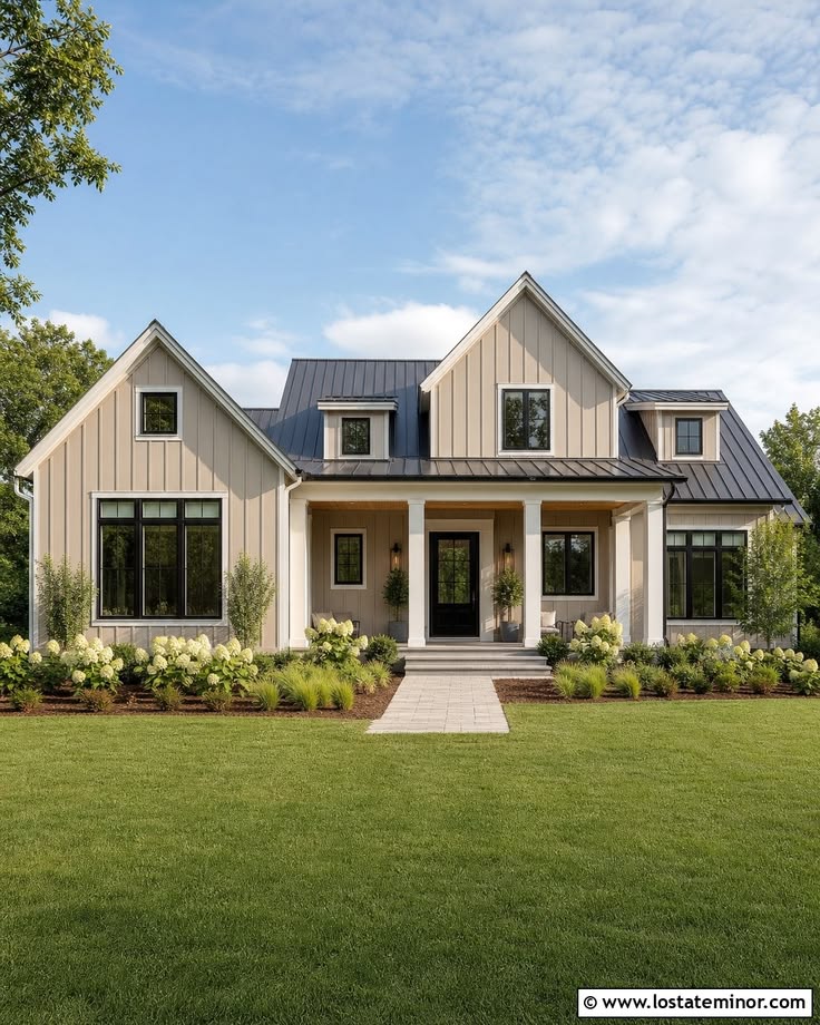 This stunning custom-built home features modern farmhouse architecture with a light beige board-and-batten siding and striking black window frames. The property boasts a symmetrical facade, a covered front porch with substantial white columns, and a dark metal roof, all set against a meticulously manicured lawn and lush hydrangeas. The overall impression is one of upscale, inviting charm and contemporary curb appeal.