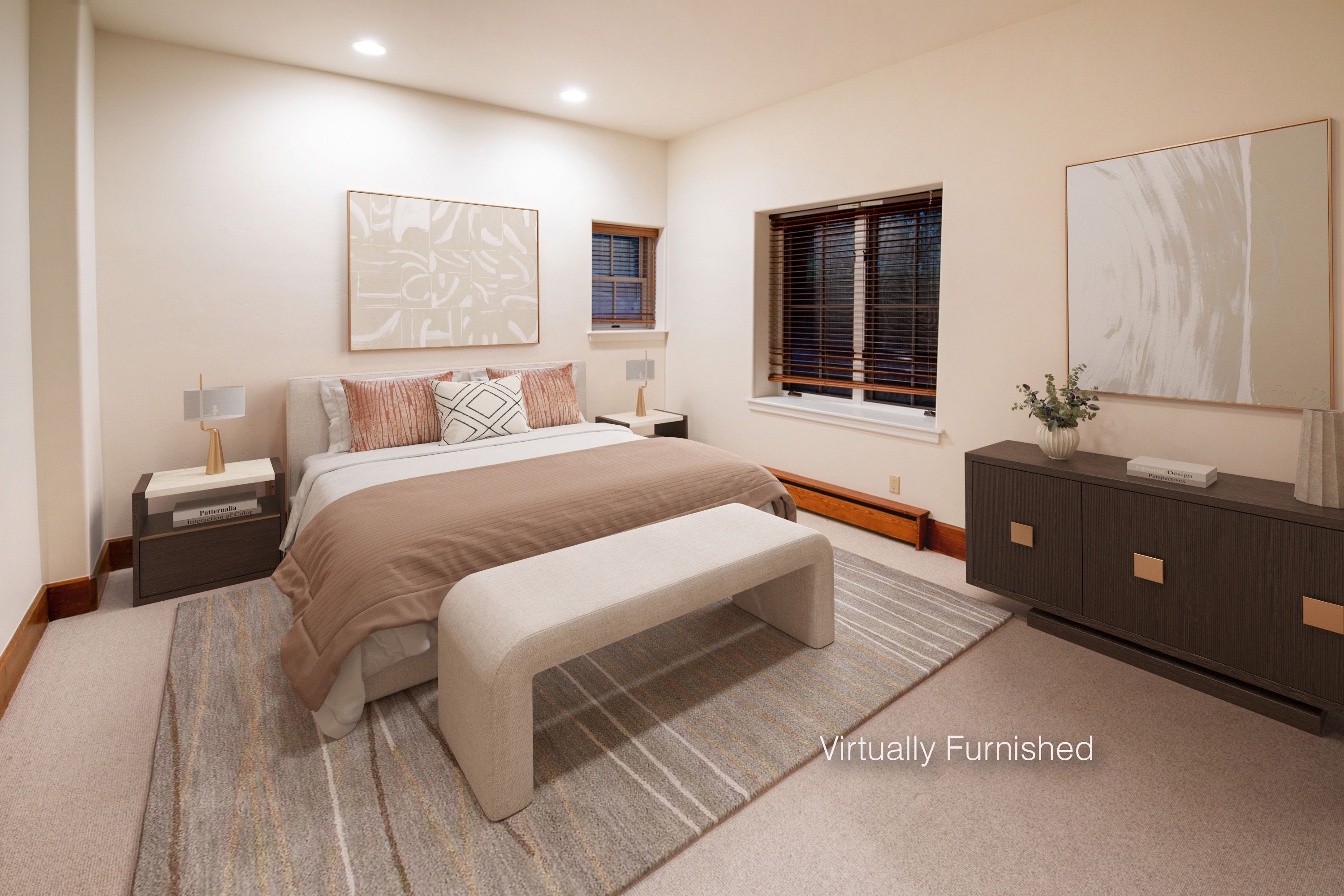 This primary bedroom features a neutral, calming color palette with a plush bed centered against a wall adorned with abstract art. A modern bench sits at the foot of the bed atop a textured area rug, while a dark wood dresser and matching nightstands provide elegant storage. The room is well-lit by recessed lighting and natural light filtering through wooden blinds, creating a serene and sophisticated atmosphere.