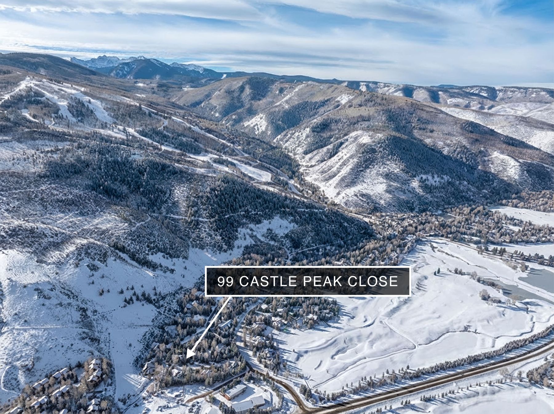 This high-altitude aerial shot captures a sprawling, snow-covered mountain landscape, highlighting the location of 99 Castle Peak Close nestled within a wooded valley. The perspective emphasizes the property's proximity to vast ski slopes, dense evergreen forests, and a nearby golf course, showcasing a premier alpine lifestyle. The scene is bathed in bright, clear daylight, emphasizing the dramatic topography and the serene, secluded nature of the residential area.