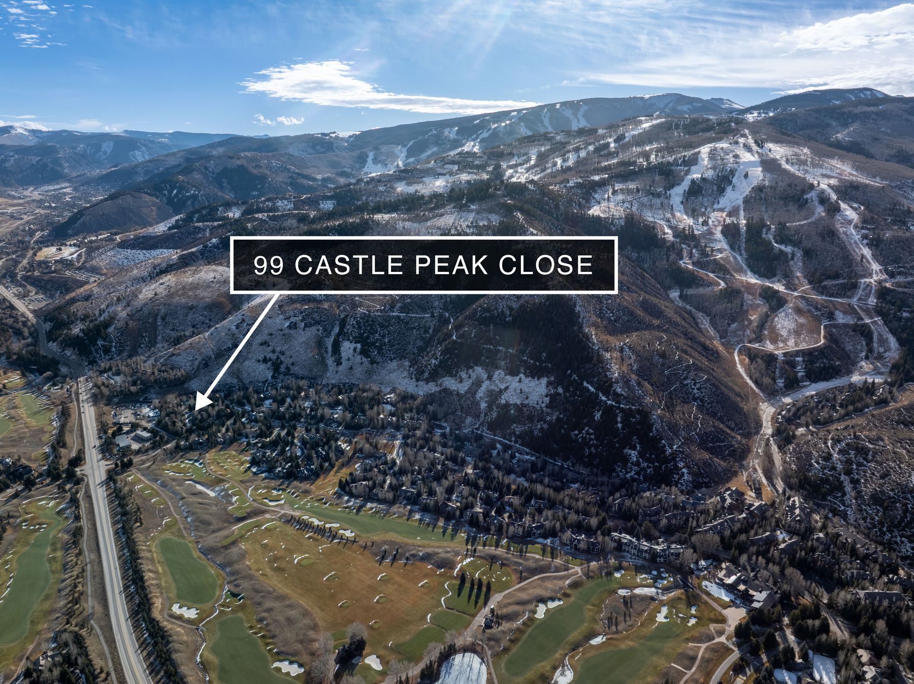 This high-altitude aerial shot captures a sprawling residential community nestled at the base of a majestic, snow-dusted mountain range. The perspective highlights the property's proximity to a lush golf course and expansive natural terrain, emphasizing a serene, upscale lifestyle. The clear blue sky and bright daylight enhance the dramatic scale of the landscape, making it an ideal showcase for a premium real estate location.