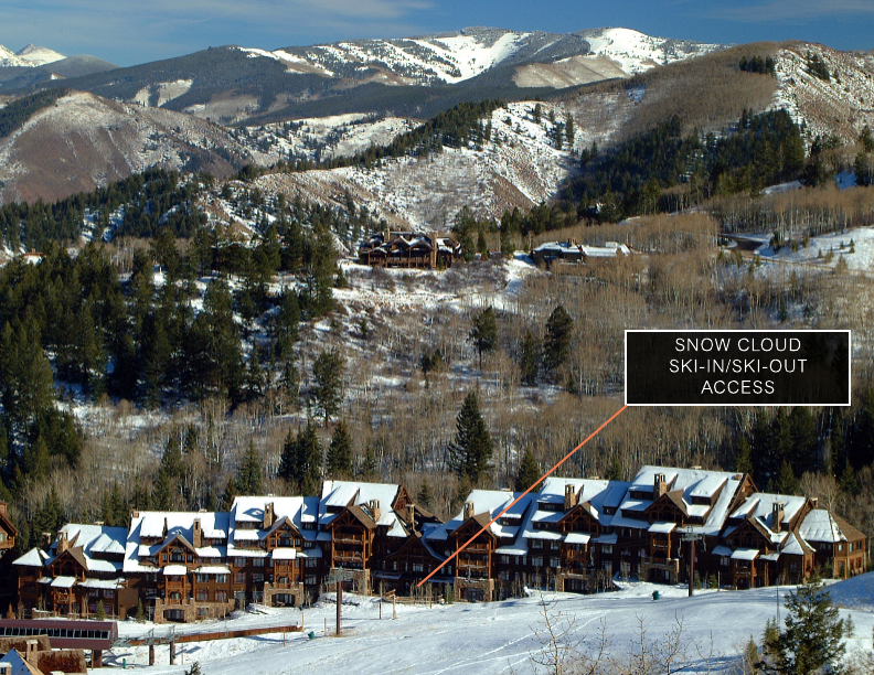 This image showcases the front view of a luxurious ski-in/ski-out condo complex nestled in a snowy mountain landscape. The architecture features a rustic-chic style with wood and stone elements, complemented by snow-covered roofs. The setting provides a sense of exclusivity and access to winter sports activities.