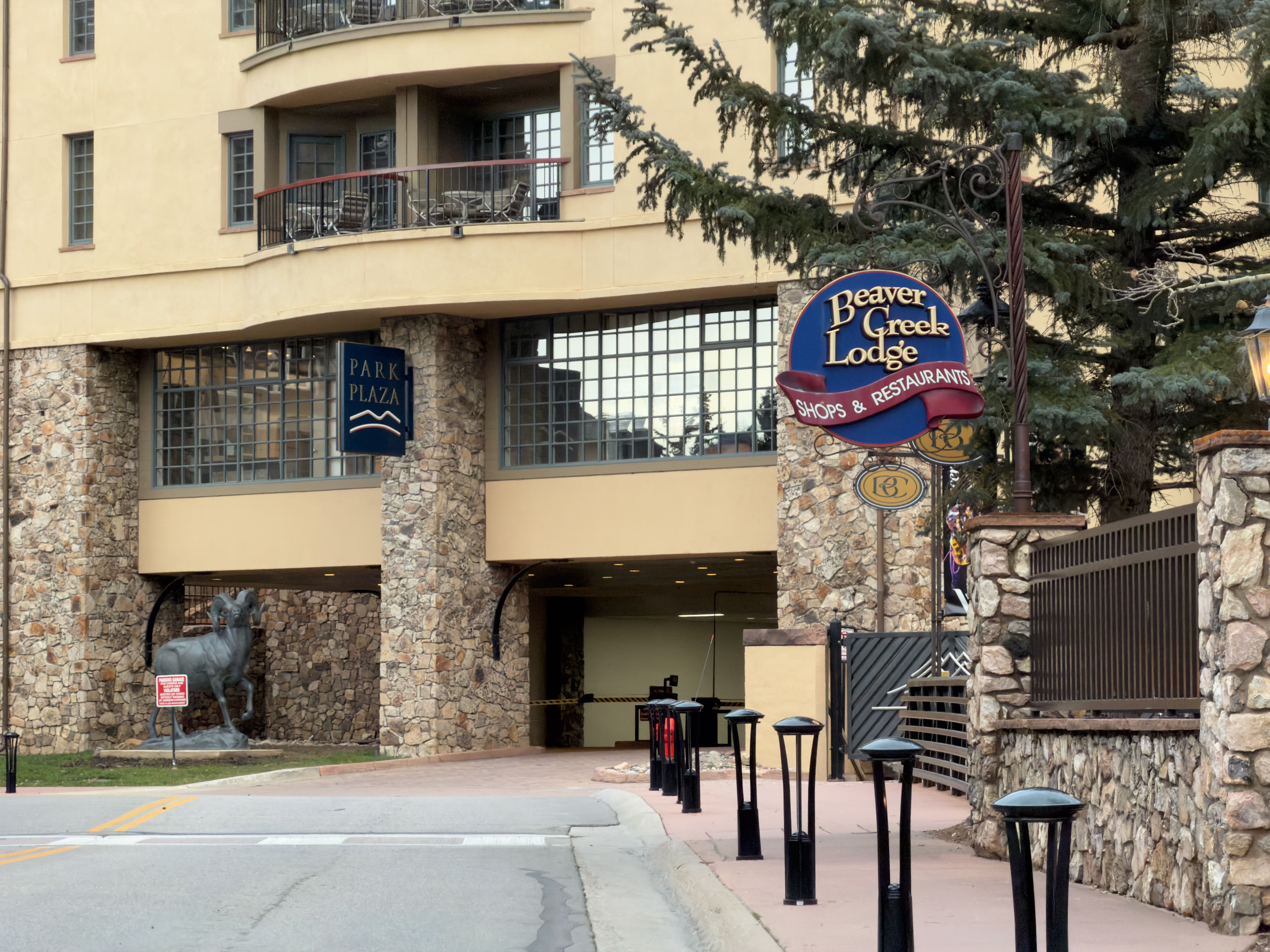 This is a front view of the Beaver Creek Lodge, showcasing its stone and stucco facade. The building features large windows, a covered entryway, and a decorative 'Beaver Creek Lodge' sign. A bronze ram statue stands near the entrance, adding a unique architectural detail.