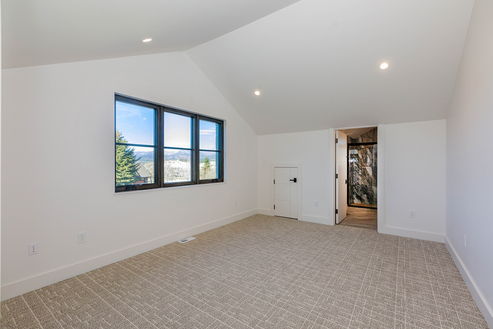 This is a bright and airy bedroom featuring neutral-toned carpet and white walls, creating a serene atmosphere. A large window provides ample natural light and a view of the outdoors. The room includes a closet and an open doorway to another room, possibly a bathroom, enhancing its functionality and appeal.