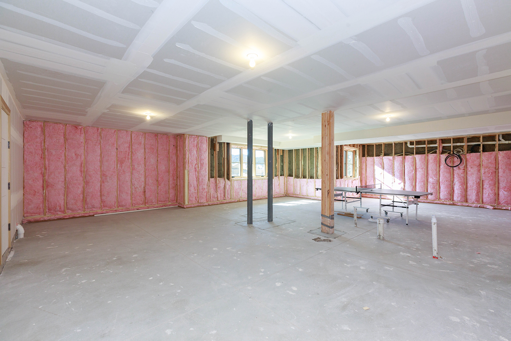 This is an unfinished basement, showcasing the potential for customization. The walls are partially insulated with pink fiberglass, and the ceiling is partially drywalled. Support beams and a concrete floor are visible, suggesting a blank canvas for future development and personalization.