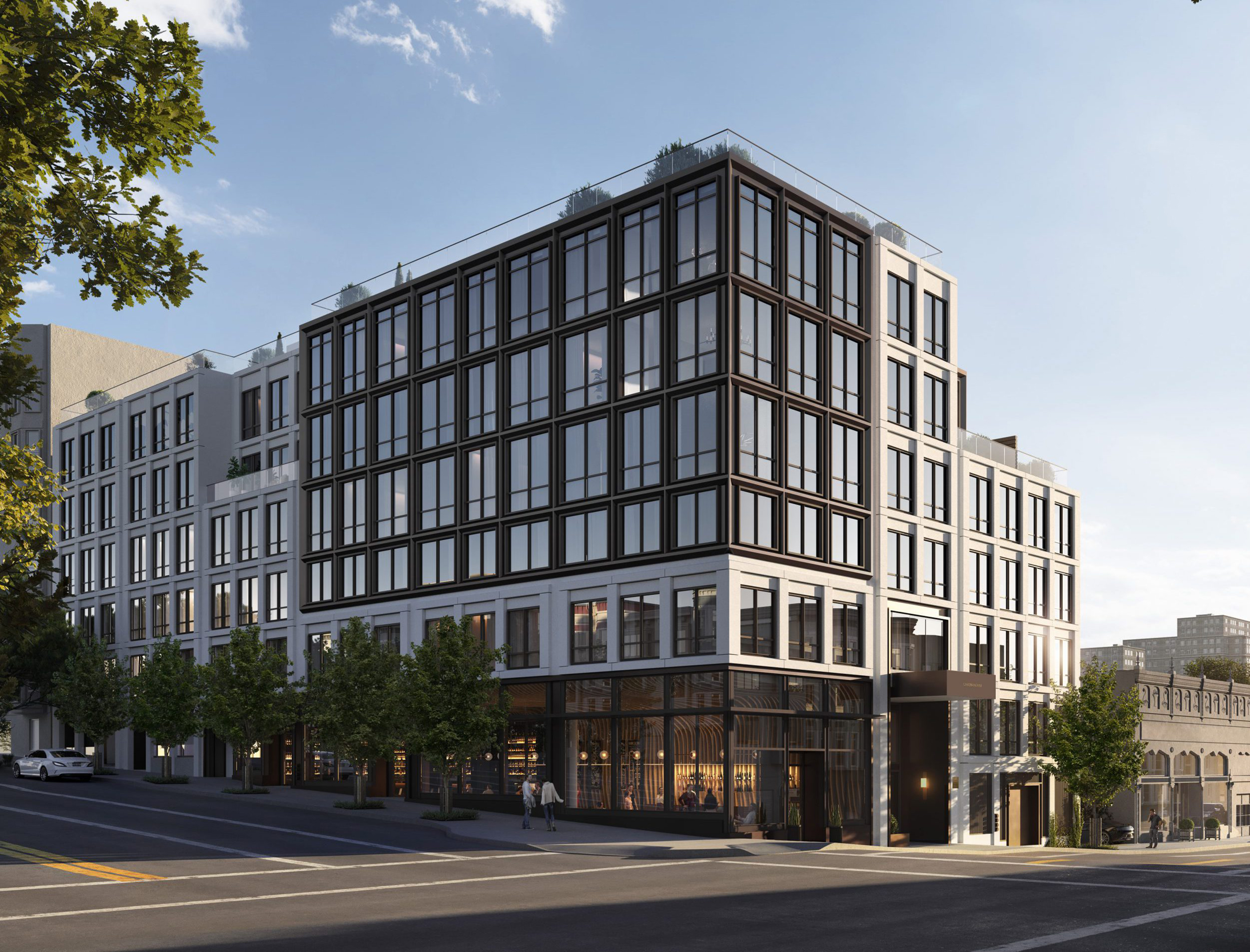 This contemporary mid-rise building showcases a sophisticated mix of white masonry and dark-framed floor-to-ceiling windows, creating a striking urban aesthetic. The street-level features a vibrant, glass-fronted commercial space with a warm, inviting interior, anchored by a prominent entrance. The architecture emphasizes a sharp, corner profile that integrates seamlessly into a cityscape environment.