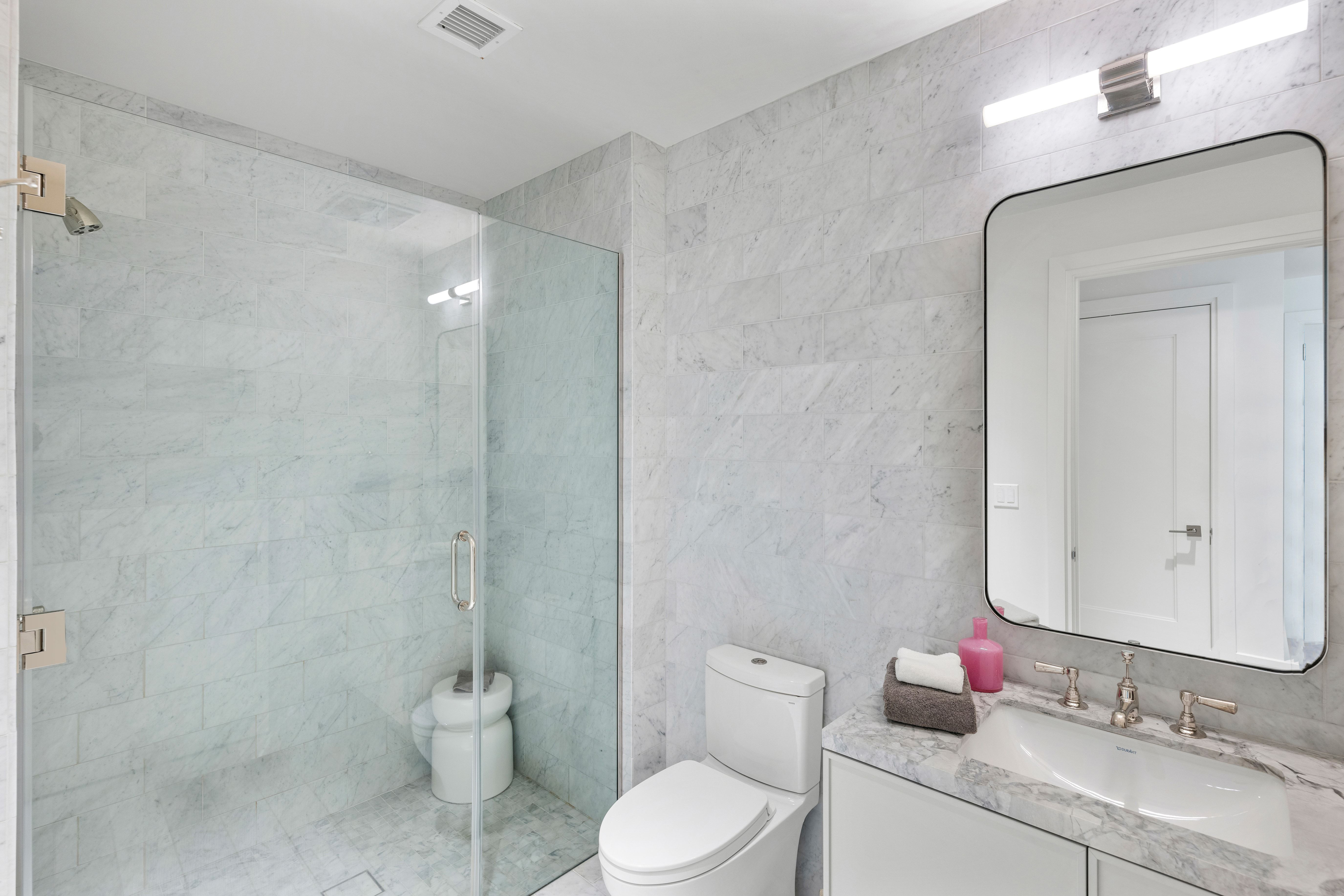 This modern primary bathroom features elegant marble tiling throughout the walls and floor, creating a cohesive and luxurious aesthetic. The space includes a sleek glass-enclosed shower, a contemporary vanity with a matching marble countertop, and high-end fixtures. A large, frameless mirror and modern lighting complete the upscale, clean design.