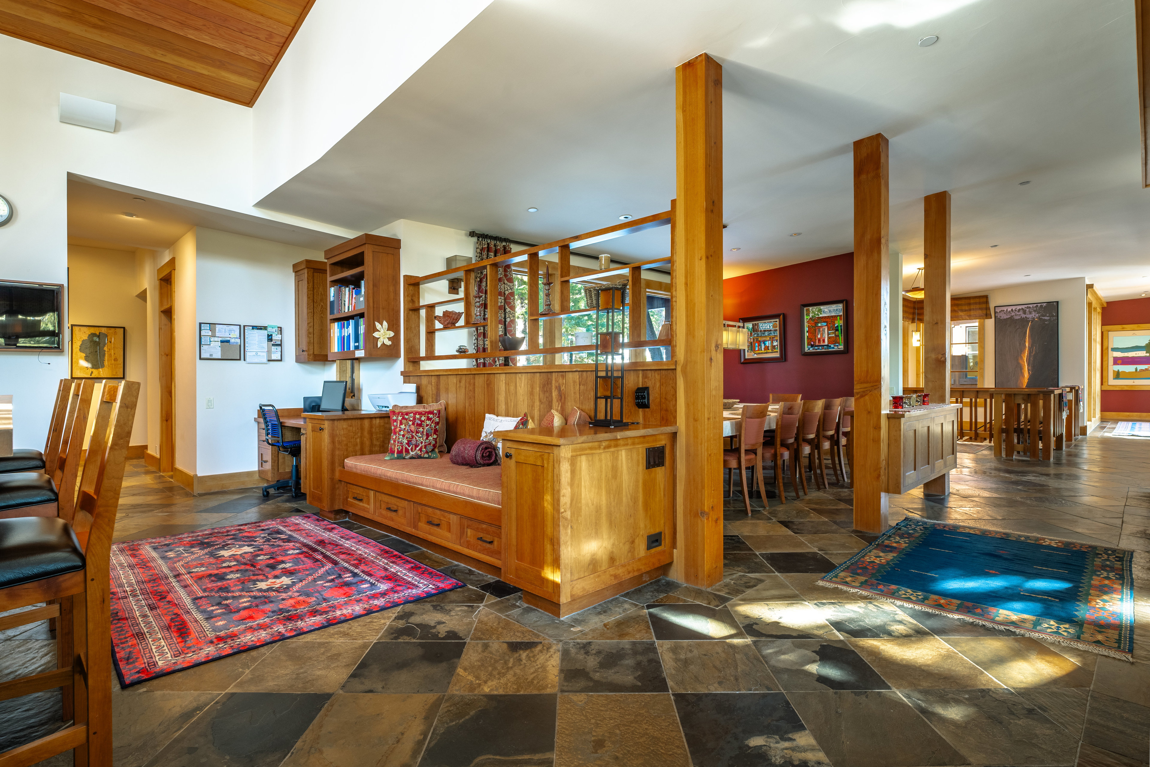 This interior shot showcases a spacious living area with a unique blend of rustic and modern design elements. The room features a built-in seating area with storage, wooden support beams, and a tiled floor. A dining area is visible in the background, suggesting an open-concept layout, and the overall impression is one of warmth and character.