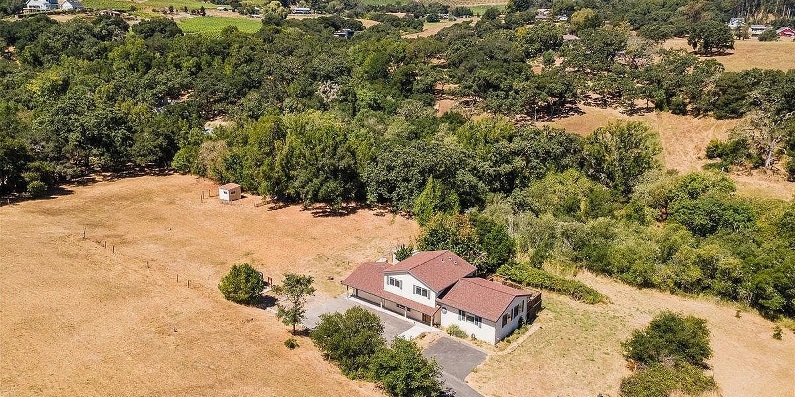 A small home surrounded by open land and mature trees, seen from above